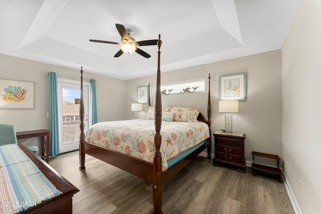 bedroom featuring access to exterior, baseboards, a raised ceiling, and dark wood-style flooring