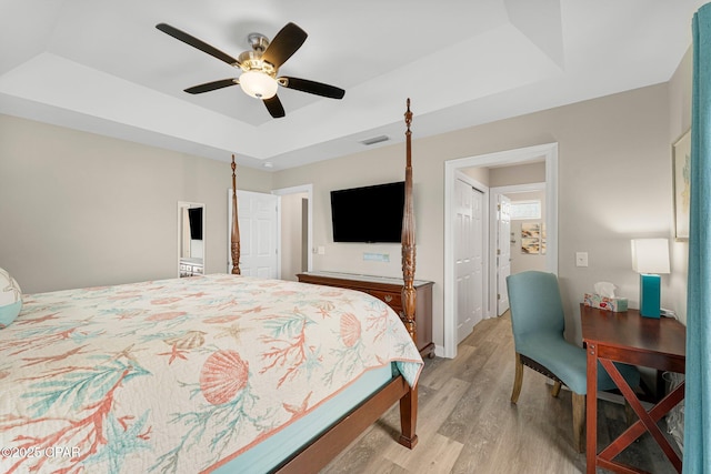 bedroom featuring light wood-style flooring, visible vents, a tray ceiling, and ceiling fan