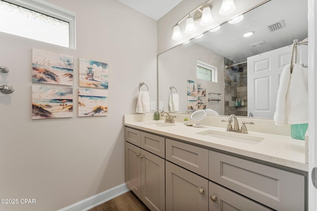 bathroom featuring double vanity, tiled shower, a sink, and visible vents