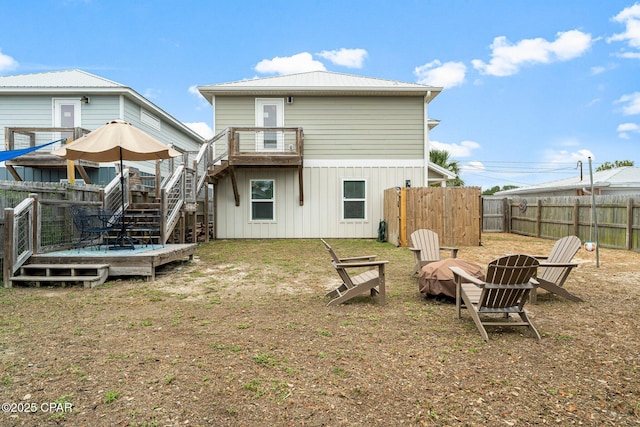 rear view of house with a deck, an outdoor fire pit, a fenced backyard, and stairs