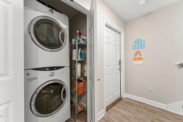 laundry area with laundry area, light wood-style flooring, baseboards, and stacked washer and clothes dryer