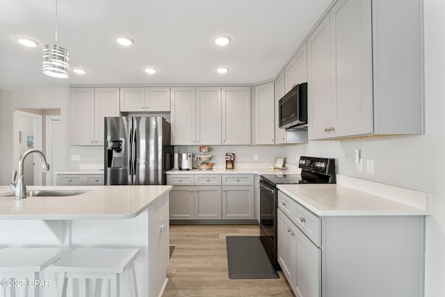 kitchen featuring light countertops, black range with electric stovetop, hanging light fixtures, a sink, and stainless steel fridge