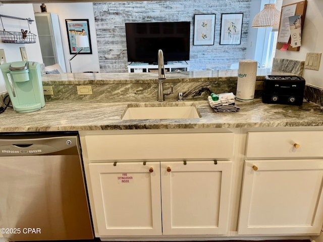 kitchen with light stone counters, dishwasher, white cabinetry, and a sink