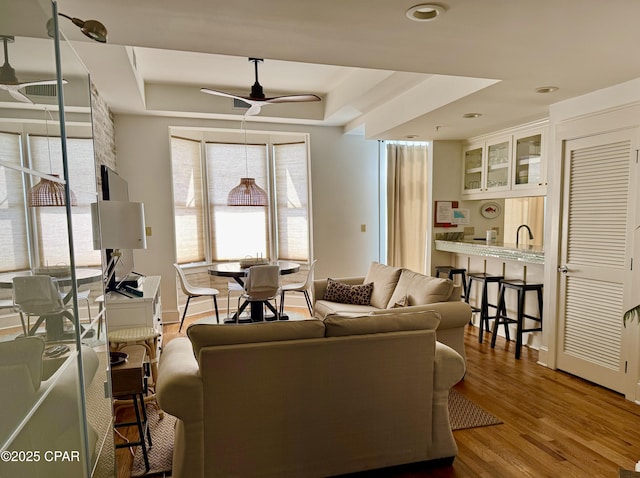 living area featuring ceiling fan, baseboards, a tray ceiling, and wood finished floors