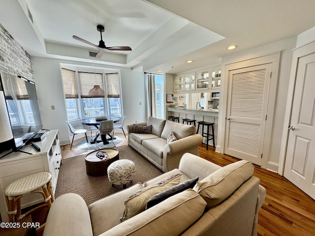 living room featuring visible vents, a raised ceiling, a ceiling fan, and wood finished floors