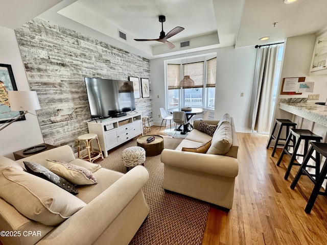 living room with an accent wall, a tray ceiling, a ceiling fan, and visible vents