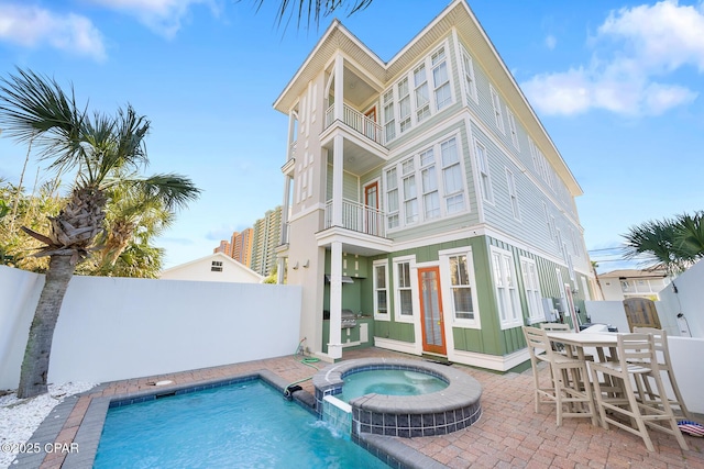 back of property with a balcony, a patio area, a pool with connected hot tub, and fence