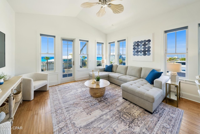 living room featuring a water view, wood finished floors, a ceiling fan, baseboards, and vaulted ceiling