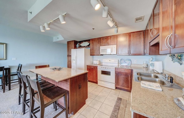 kitchen with sink, white appliances, a breakfast bar area, light tile patterned floors, and light stone countertops