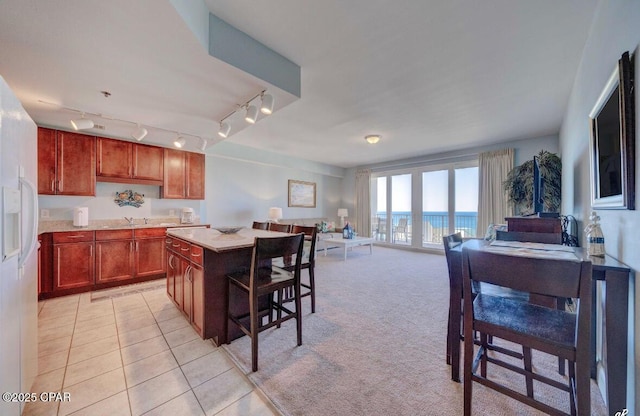 kitchen featuring a kitchen bar, white refrigerator with ice dispenser, a center island, light colored carpet, and a water view