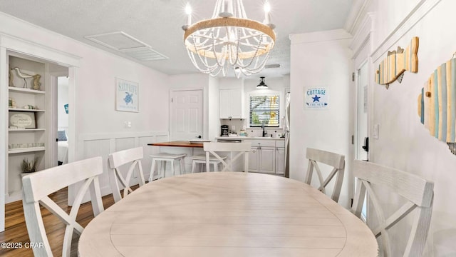 dining area with sink, built in features, a notable chandelier, light hardwood / wood-style floors, and a textured ceiling