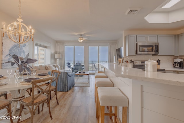 kitchen with light hardwood / wood-style flooring, gray cabinets, appliances with stainless steel finishes, tasteful backsplash, and light stone countertops