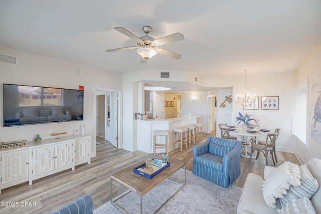 living room with ceiling fan with notable chandelier and light hardwood / wood-style flooring