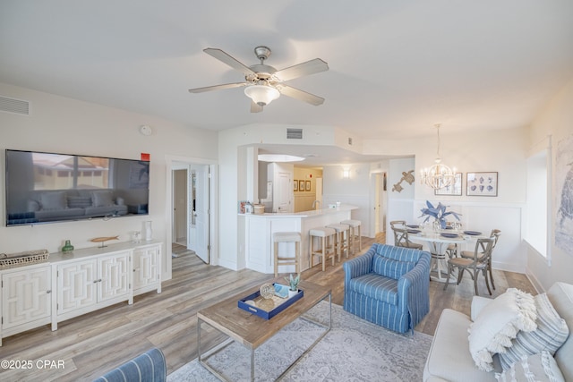 living room featuring ceiling fan with notable chandelier and light hardwood / wood-style flooring