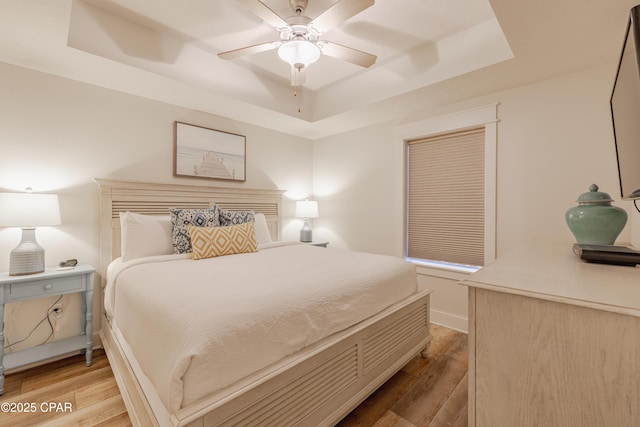 bedroom with light hardwood / wood-style floors, a raised ceiling, and ceiling fan