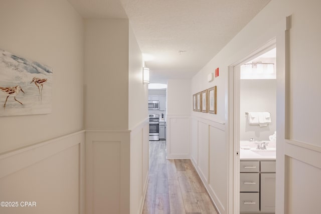 corridor featuring sink, light hardwood / wood-style floors, and a textured ceiling