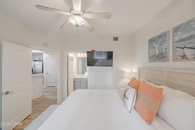 bedroom featuring stainless steel refrigerator with ice dispenser, ceiling fan, ensuite bathroom, and light hardwood / wood-style floors