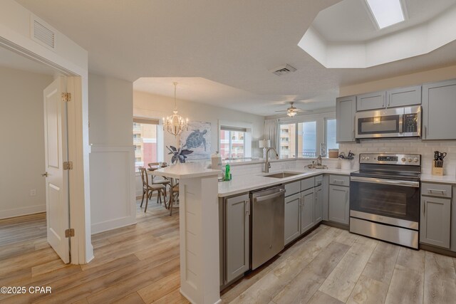 kitchen with light hardwood / wood-style floors, appliances with stainless steel finishes, kitchen peninsula, and sink