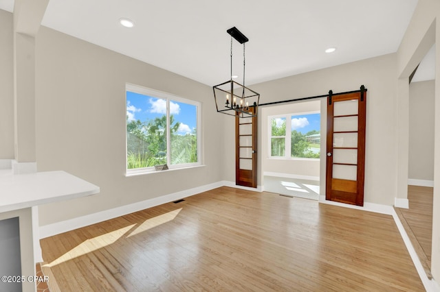 unfurnished dining area with a barn door, a chandelier, and light hardwood / wood-style floors