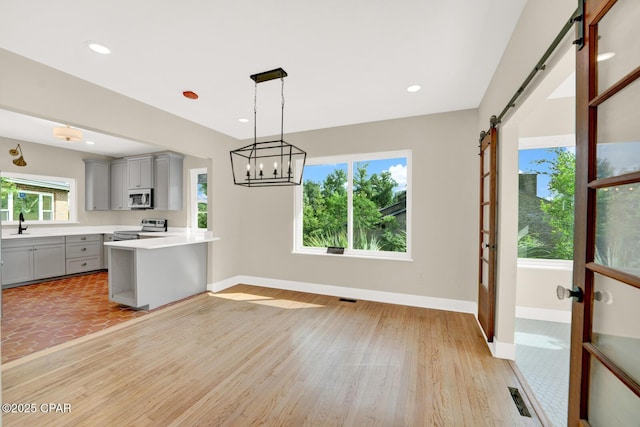 kitchen featuring pendant lighting, light hardwood / wood-style flooring, appliances with stainless steel finishes, gray cabinetry, and a barn door