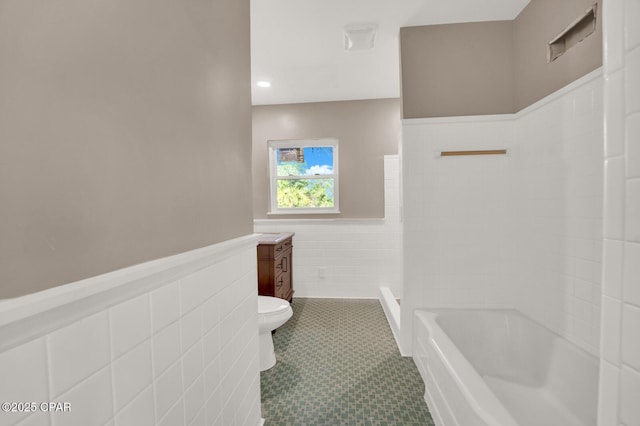 bathroom with vanity, tile walls, a bathtub, and toilet