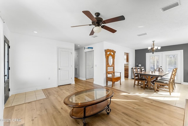 living area with light wood-type flooring, baseboards, visible vents, and ceiling fan with notable chandelier