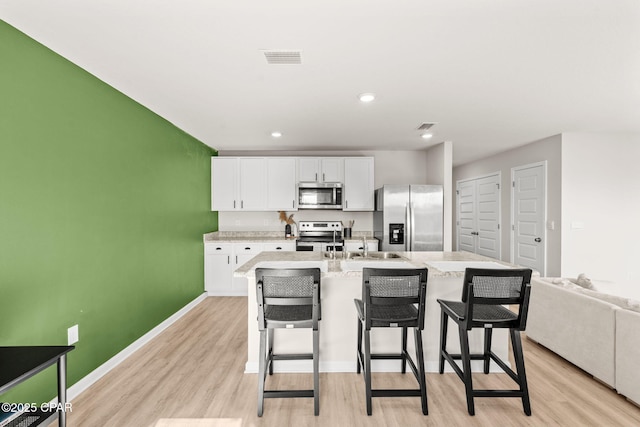 kitchen with a kitchen bar, a center island with sink, appliances with stainless steel finishes, light hardwood / wood-style floors, and white cabinets