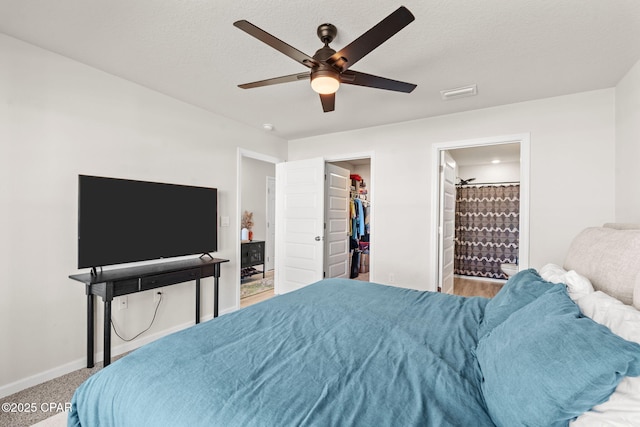 bedroom featuring a walk in closet, ensuite bath, a textured ceiling, carpet floors, and ceiling fan