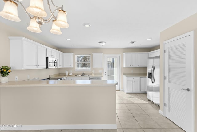 kitchen with light tile patterned floors, appliances with stainless steel finishes, hanging light fixtures, white cabinets, and kitchen peninsula