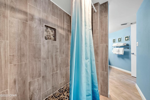 bathroom with wood finished floors, a tile shower, and baseboards