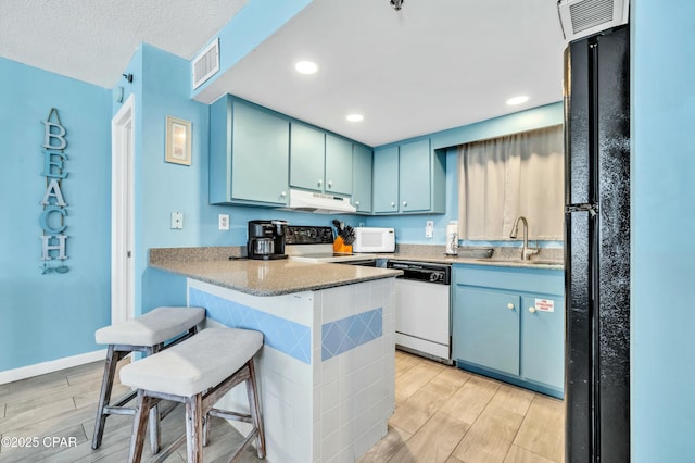 kitchen with white appliances, wood finish floors, blue cabinetry, and under cabinet range hood