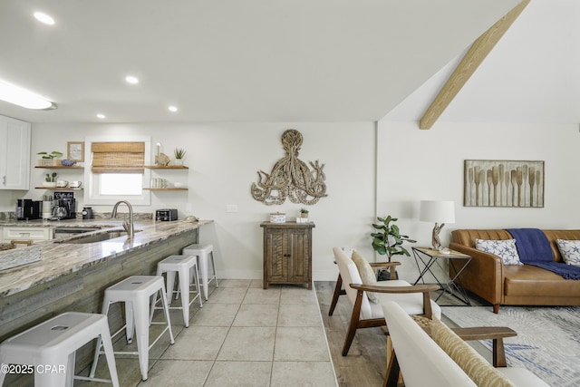 kitchen with light stone counters, a breakfast bar area, open shelves, white cabinetry, and a sink