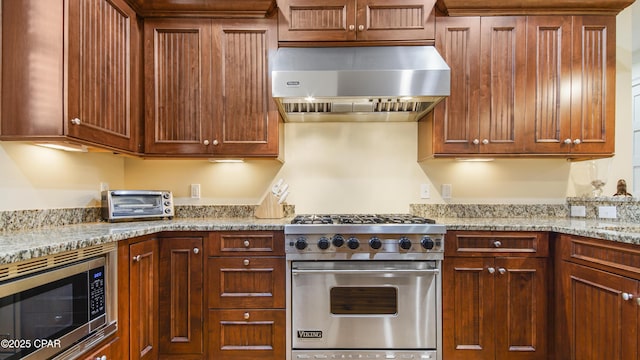 kitchen with light stone countertops, a toaster, stainless steel appliances, wall chimney range hood, and brown cabinets