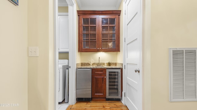 bar with wine cooler, stainless steel dishwasher, light wood-style floors, ornamental molding, and washer / dryer