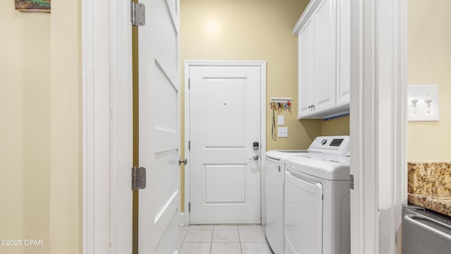 clothes washing area featuring light tile patterned floors, washing machine and dryer, and cabinet space