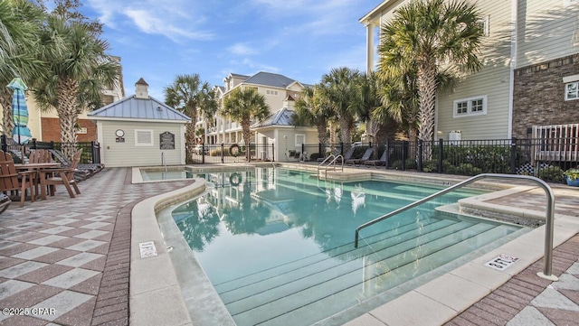 community pool with an outbuilding, a patio area, and fence