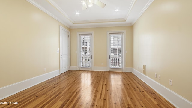 unfurnished room with a ceiling fan, baseboards, ornamental molding, a tray ceiling, and light wood finished floors