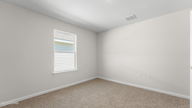 carpeted spare room featuring a wealth of natural light, visible vents, and baseboards