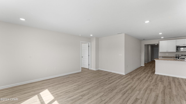 kitchen with light wood finished floors, baseboards, white cabinets, stainless steel microwave, and stove