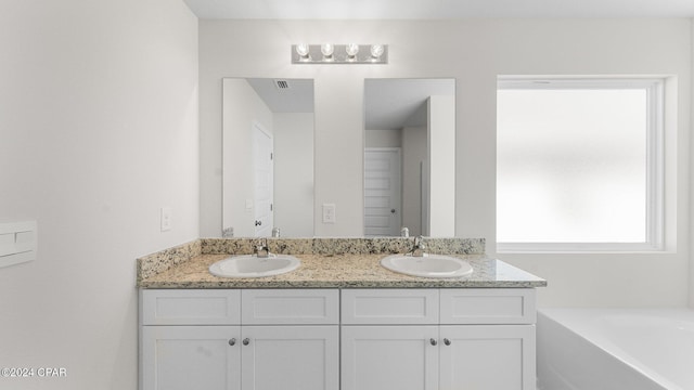 bathroom with a garden tub, double vanity, a sink, and visible vents