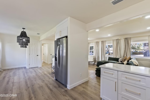 kitchen featuring stainless steel refrigerator with ice dispenser, white cabinetry, pendant lighting, and light wood-type flooring