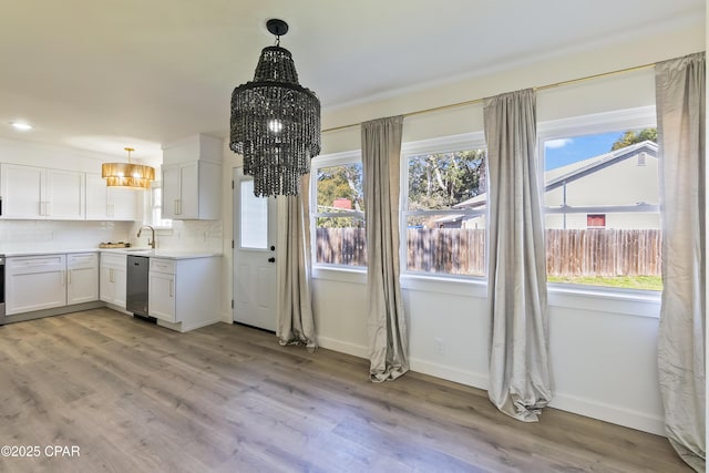 kitchen featuring pendant lighting, white cabinetry, decorative backsplash, stainless steel dishwasher, and light hardwood / wood-style floors