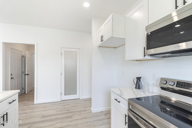 kitchen with white cabinets, light wood-type flooring, appliances with stainless steel finishes, and baseboards