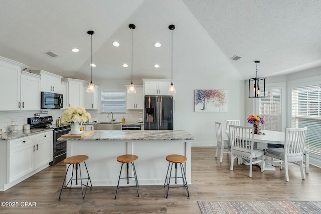 kitchen featuring white cabinetry, hanging light fixtures, a kitchen island, light stone countertops, and black appliances