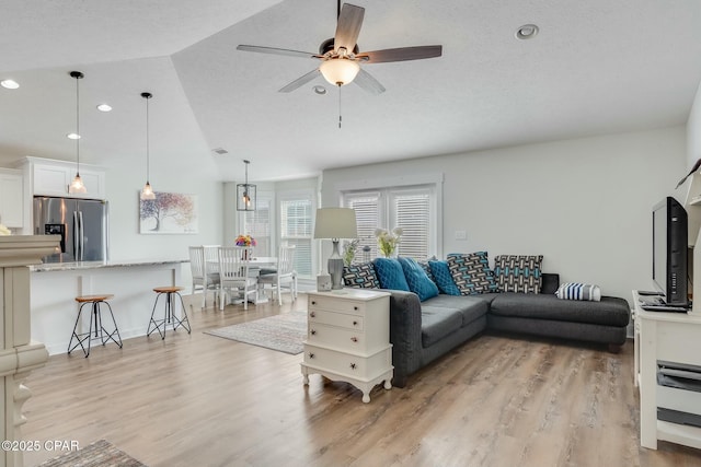 living room featuring vaulted ceiling, ceiling fan, light hardwood / wood-style floors, and a textured ceiling