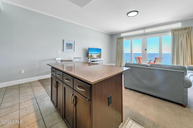 kitchen featuring light tile patterned floors, a kitchen island, dark brown cabinets, crown molding, and open floor plan