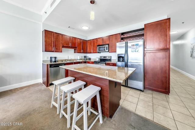 kitchen with a breakfast bar area, light tile patterned floors, a kitchen island, a sink, and appliances with stainless steel finishes