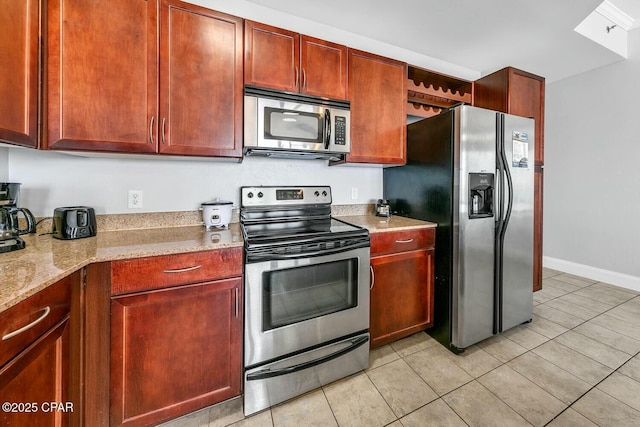 kitchen featuring appliances with stainless steel finishes, light stone countertops, and reddish brown cabinets