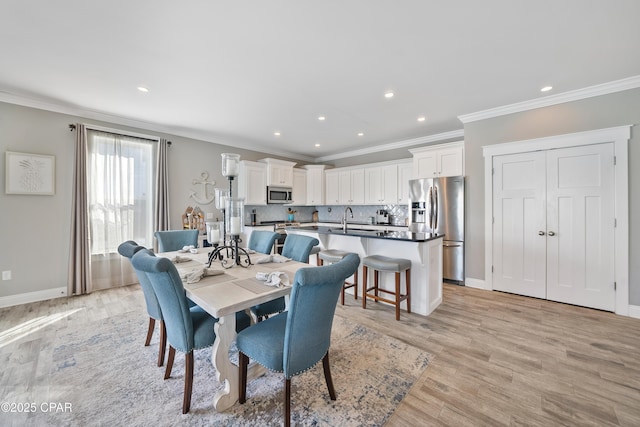 dining space with ornamental molding, sink, and light wood-type flooring