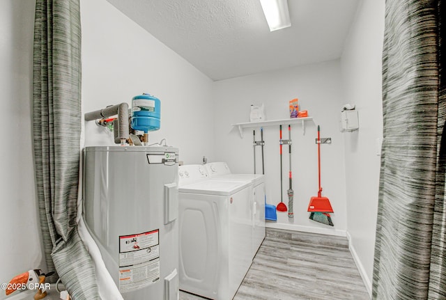 washroom featuring washing machine and dryer, electric water heater, a textured ceiling, and light hardwood / wood-style floors